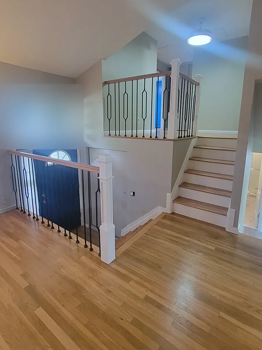 Staircase remodel in Port Washington, NY: a refinished wood floor leading to split-level stairs with white posts and black metal spindles