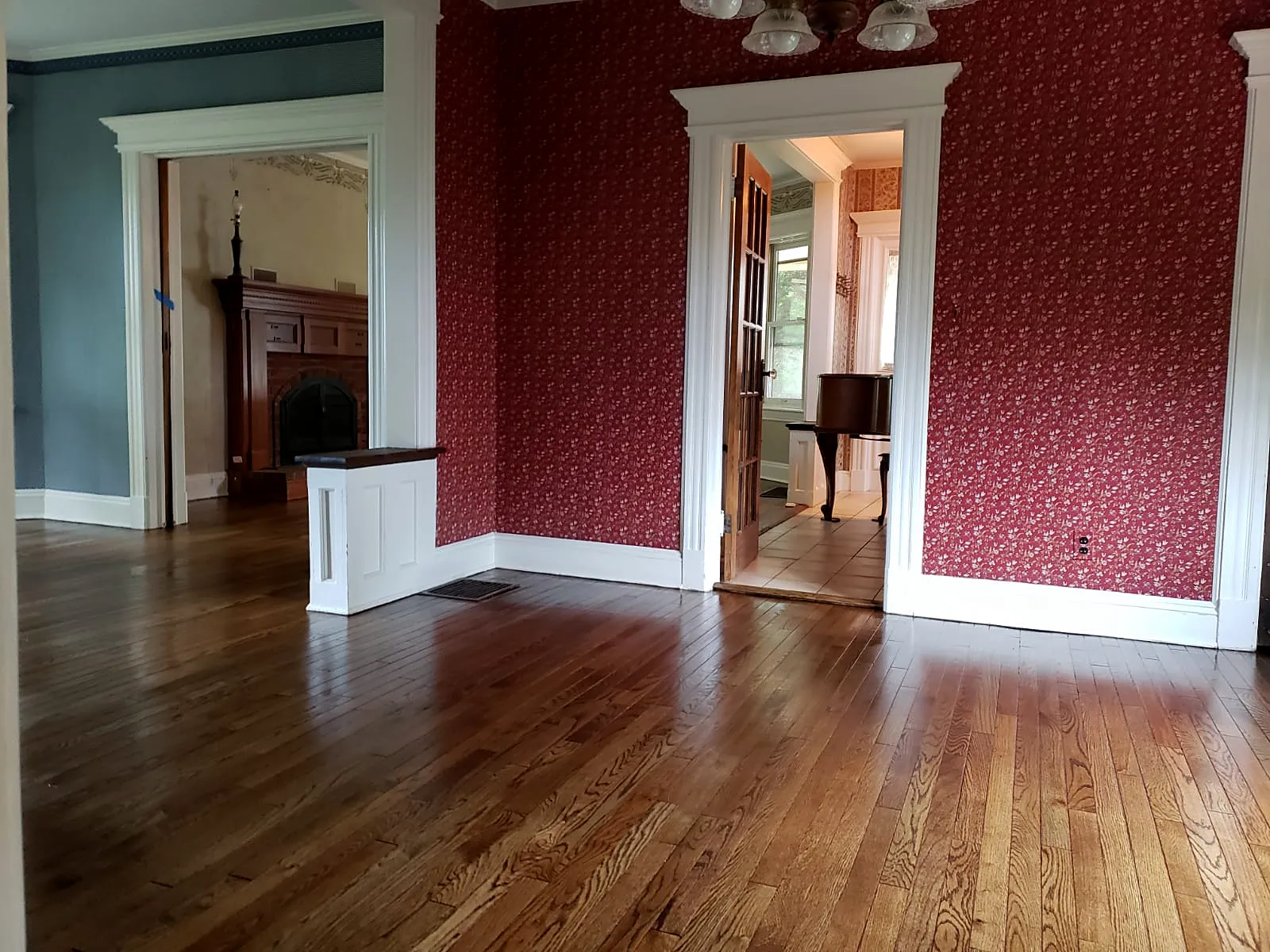 Living room remodel in Rockville Centre, NY: a refinished wood floor in a room with red patterned wallpaper and white door casings