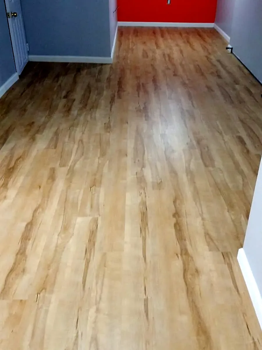 Basement remodel in Roosevelt, NY: a light wood-look vinyl plank floor running through a long basement room with an orange accent wall