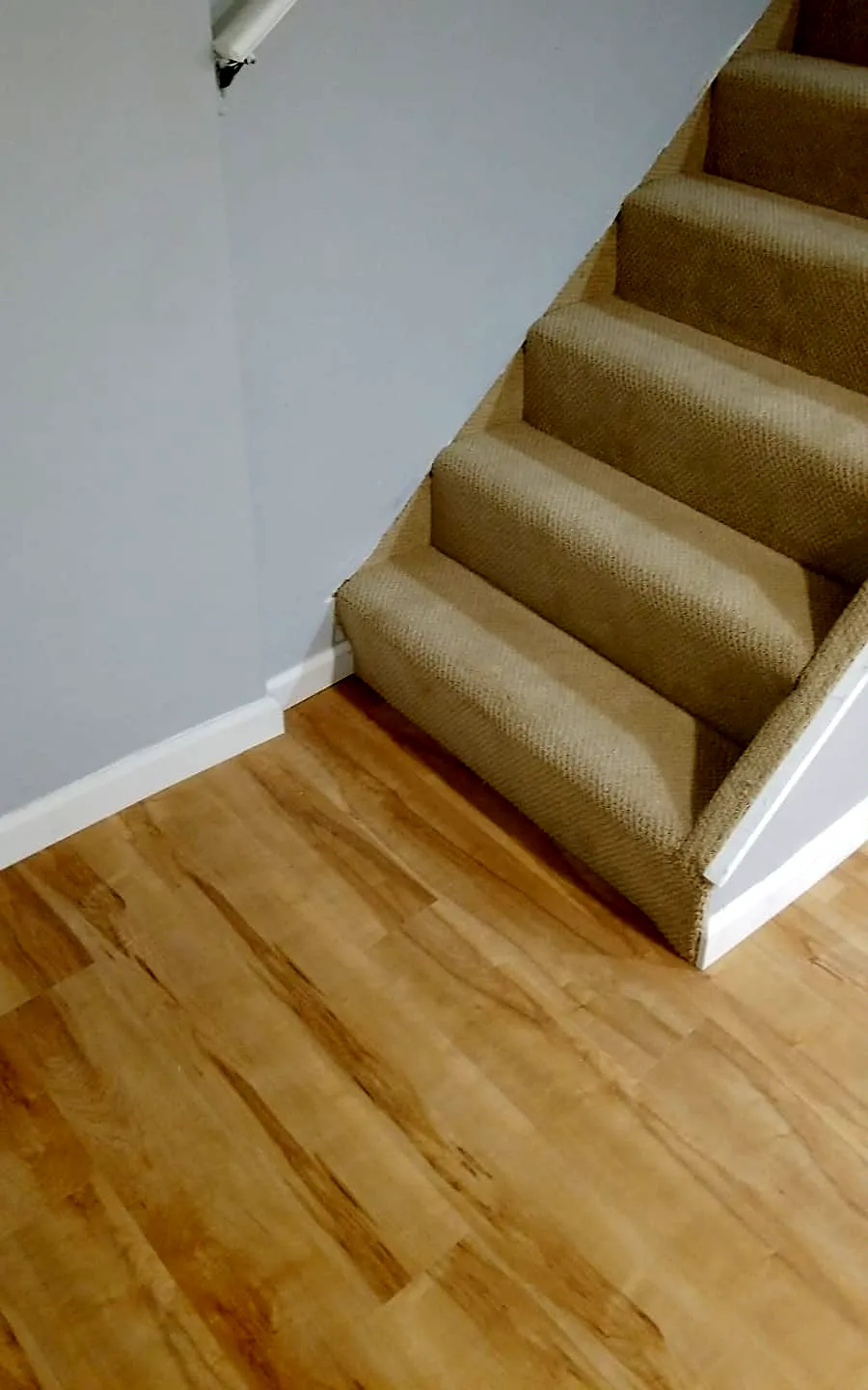 Basement staircase remodel in Roosevelt, NY: beige carpeted basement stairs meeting a light wood-look vinyl plank floor