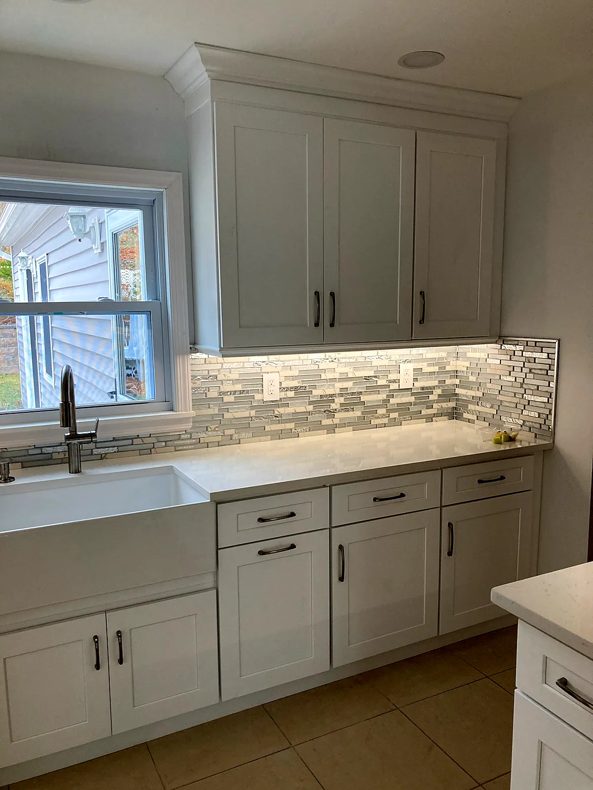 Kitchen remodel in Smithtown, NY: white shaker cabinets with a farmhouse sink, light counters and a glass mosaic backsplash