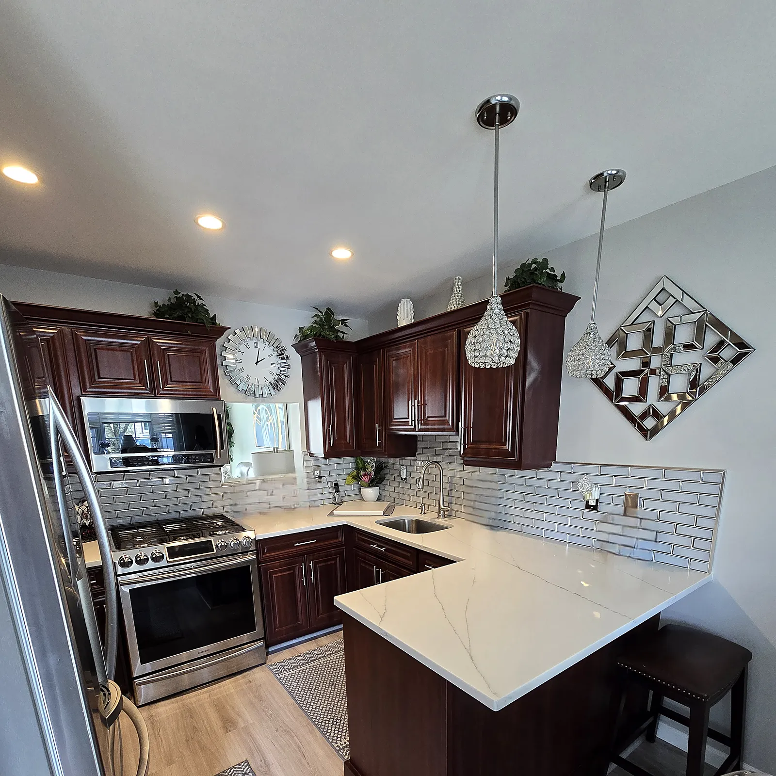 Kitchen remodel in Uniondale, NY: cherry cabinets with a white marble-look peninsula, a white subway backsplash and pendant lights