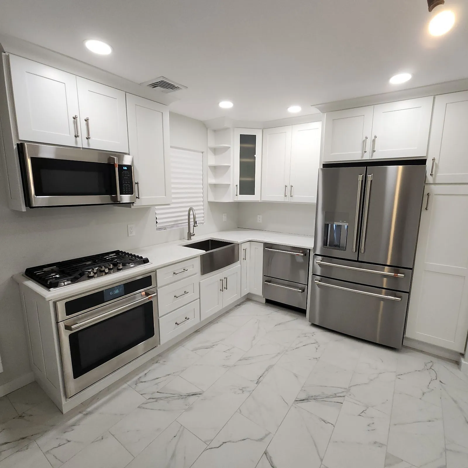 Kitchen remodel in West Babylon, NY: a white shaker kitchen with stainless appliances, a farmhouse sink and marble-look floor tile