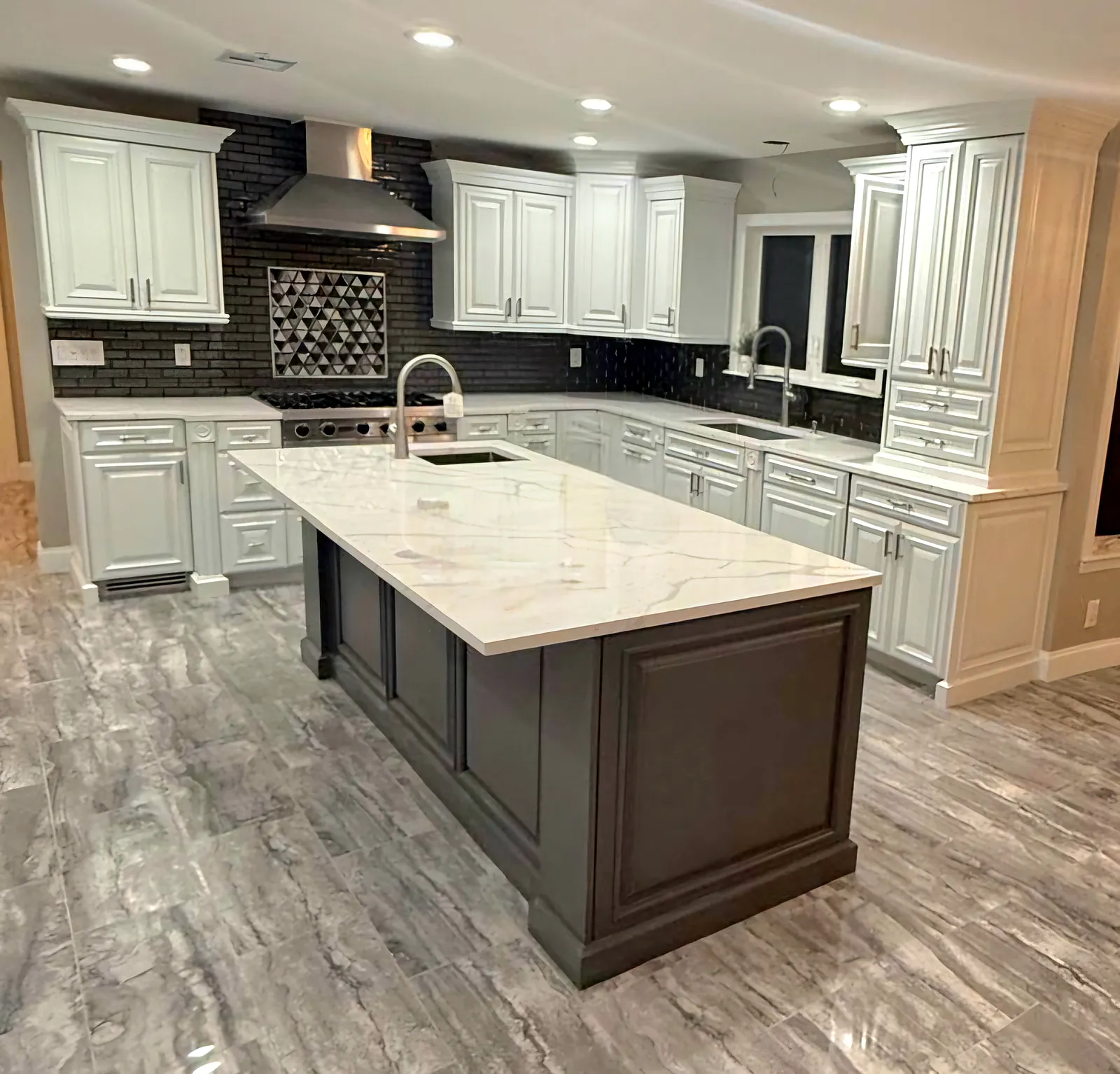Kitchen remodel in Woodbury, NY: a white kitchen with a gray island, a white stone-look top, a black tile backsplash and a steel hood